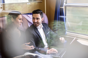 A photo of two people working on their laptops while on a train journey