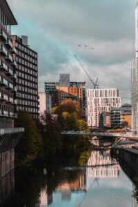 Street scene in Manchester. Tall buildings overlooking a tree lined river with a crane in the background.